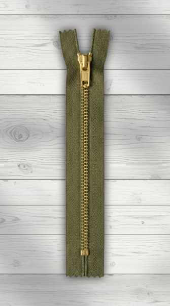 Olivfarbener Jeansreißverschluss mit goldener Metallraupe auf hellem Holzhintergrund, geschlossen.