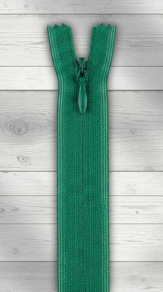 Grüner nahtverdeckter Reißverschluss auf hellem Holzhintergrund, geschlossen — die Raupe ist nach innen eingerollt und kaum sichtbar.