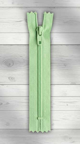 Hellgrüner Standardreißverschluss mit Kunststoffraupe, geschlossen, auf hellem Holzhintergrund.
