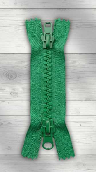 Grüner Zweiwege-Reißverschluss mit zwei Schiebern auf hellem Holzhintergrund, teilbar, von beiden Seiten zu öffnen.