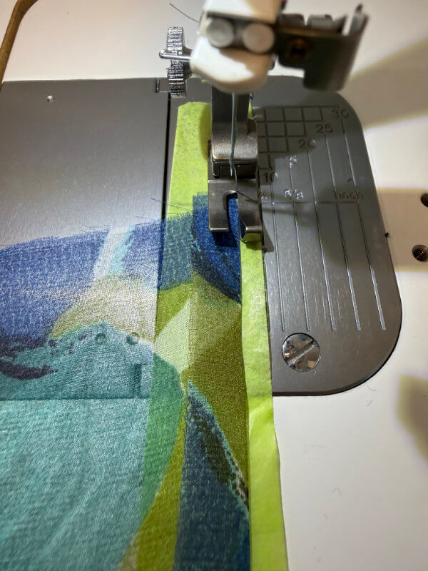 Nähmaschinen-Nähfuß gleitet über blau-gemusterten Stoff mit grünem Seidenpapier als Unterlage