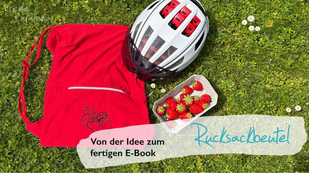 Selbst genähter roter Rucksackbeutel mit aufgestickter Erdbeere, Fahrradhelm und frischen Erdbeeren auf einer Wiese