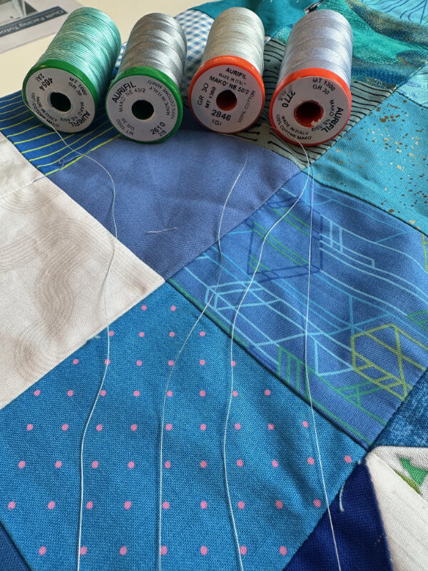 Mehrere Garnrollen liegen aufgereiht auf einem blauen Quilt