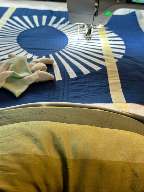 Blauer Quilt an der Nähmaschine liegt auf einem Kissen auf dem Schoß auf, Malerkrepp als Führung für gerade Linien