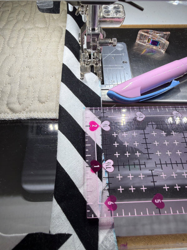 schwarz-weiß gestreiftes Binding wird mit der Nähmaschine an die Kante eines grauen Quilts genäht