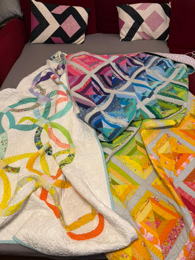 Zwei fertige Patchwork-Quilts liegen zum Zudecken auf einem Bett, dazu passende gequiltete Kissen