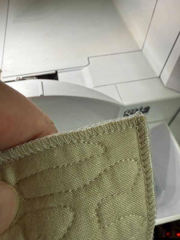 Ecke eines Quilts mit umlaufender Overlocknaht, die die drei Lagen vor dem Annähen des Bindings sichert