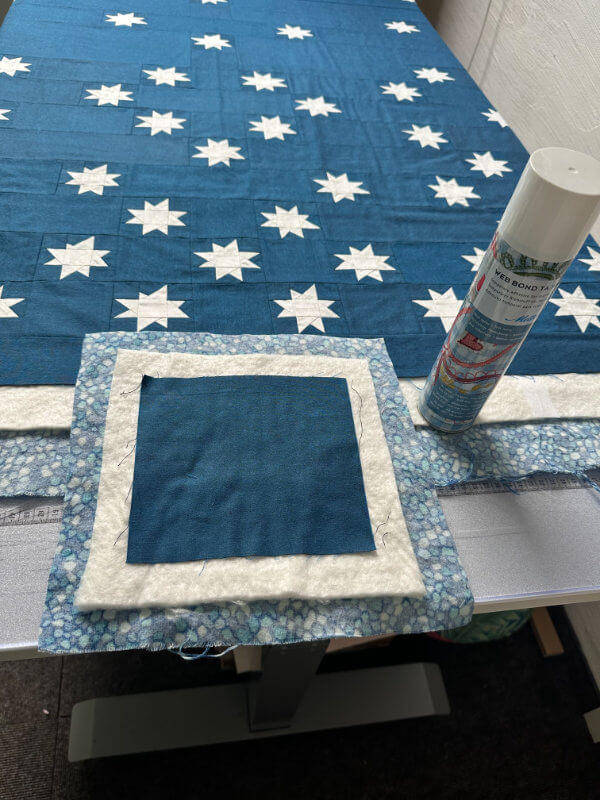 Ein Quilt mit weißen Sternen auf dunkelblauem Grund wird mit Sprühkleber zum Quiltsandwich fixiert, Sprühdose daneben