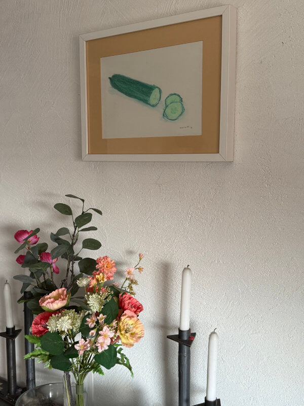 Gerahmte Zeichnung einer Gurke mit zwei Scheiben, gemalt von Anja Dix, im Esszimmer über einem Blumenstrauß