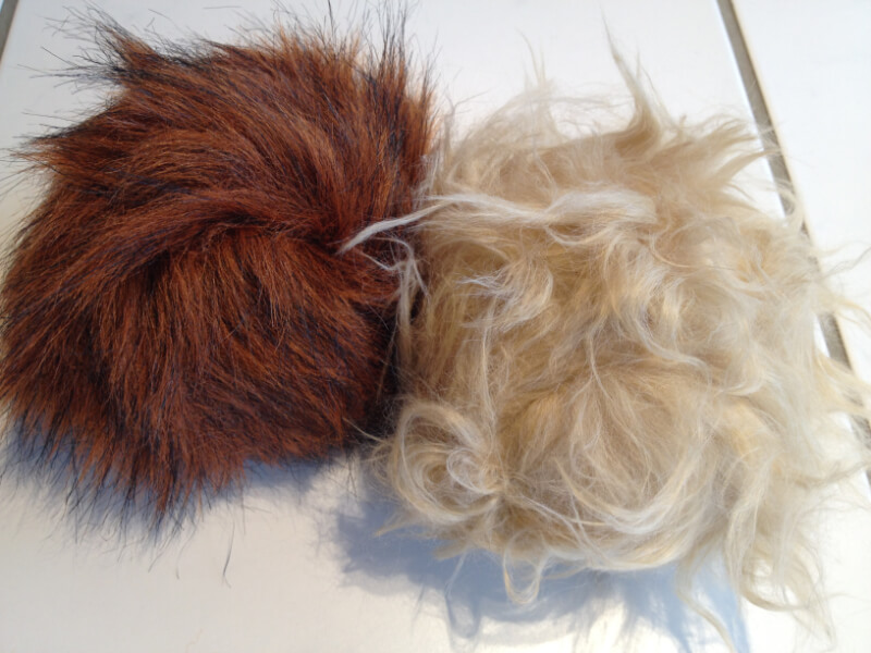 Zwei runde Tribbles aus Kunstfell, einer rotbraun mit dunklen Spitzen, einer hellbeige mit lockigem Flor, auf einem weißen Tisch