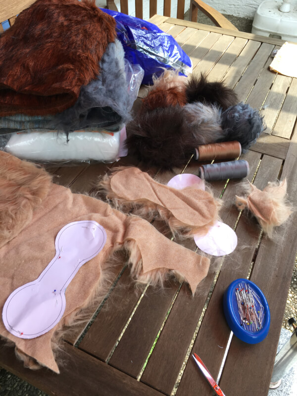 Gartentisch mit Kunstfell in verschiedenen Farben, einem knochenförmigen Papierschnitt mit Stecknadeln, Füllwatte, Garnrollen und fertigen Fellbällen